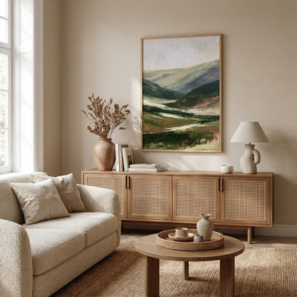 a cozy living room with a large painting of a mountain landscape hanging on the wall above a wooden cabinet. The room is furnished with a beige sofa, a wooden coffee table, and a lamp on a side table. The overall decor has a warm and inviting atmosphere.