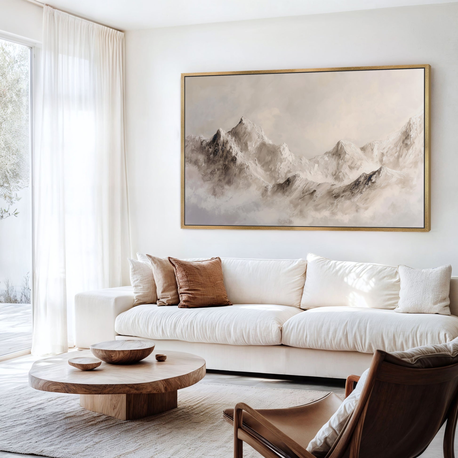 a serene living room with a large, framed painting of a mountain landscape hanging on the wall. The room is furnished with a white sofa, a wooden coffee table, and a brown leather armchair. The overall color scheme of the room is neutral, with white walls and a wooden floor.