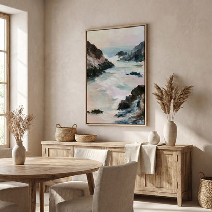 a serene dining room with a large painting of a rocky coastline hanging on the wall above a wooden table and chairs. The room has a neutral color palette, with a large window providing natural light and a view of the outdoors. The dining table is set with a vase of dried flowers and a woven basket, adding a touch of nature and rustic charm to the space.