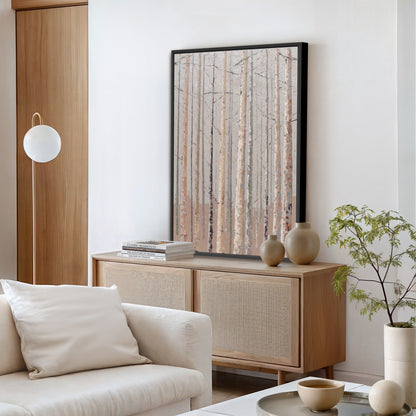 a modern living room with a large framed picture of a forest scene hanging on the wall above a wooden cabinet. The room is furnished with a white sofa, a coffee table, and a potted plant, creating a serene and inviting atmosphere.