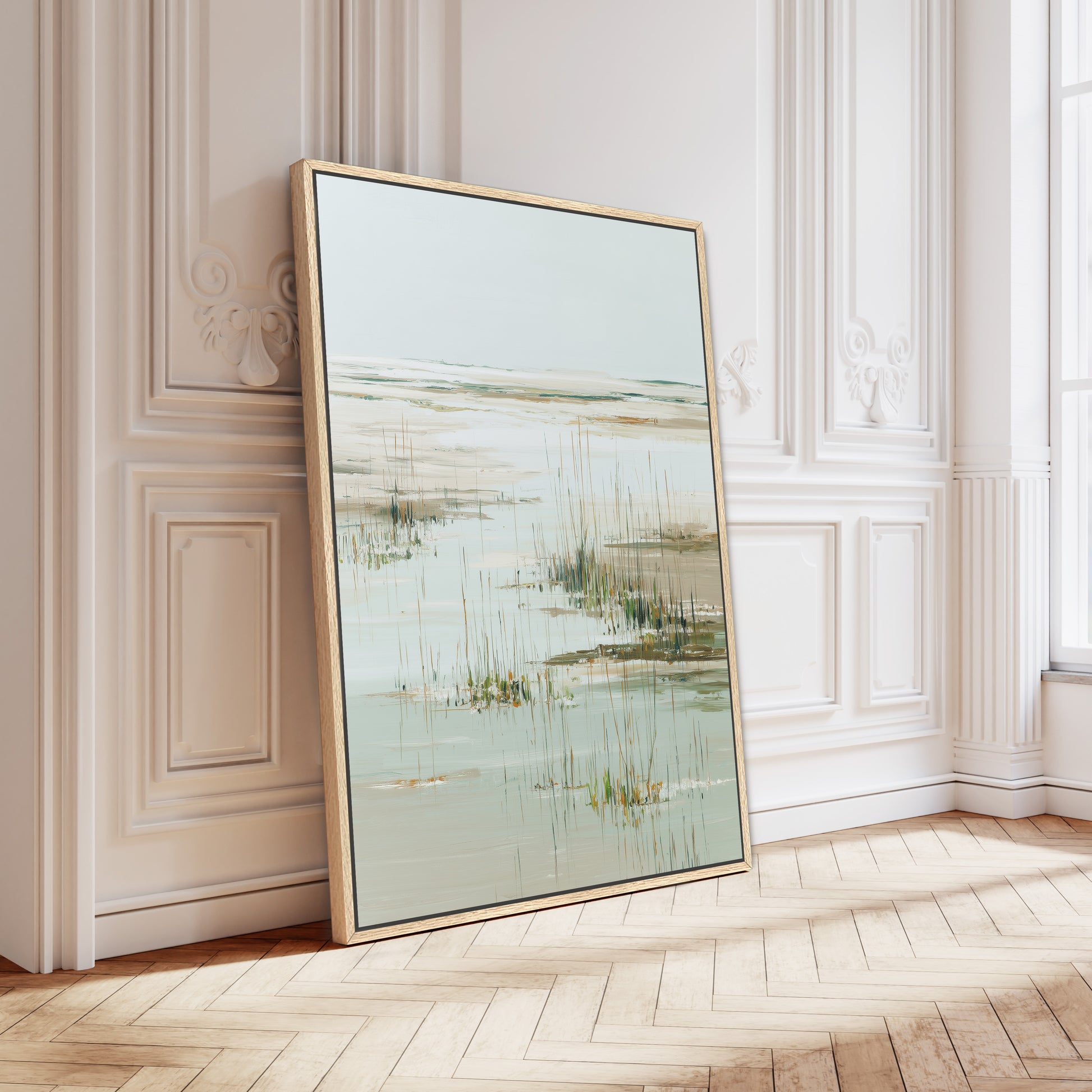 a large framed painting of a serene landscape with a body of water and tall grasses, displayed on a wooden floor against a white wall.