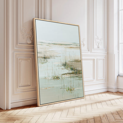 a large framed painting of a serene landscape with a body of water and tall grasses, displayed on a wooden floor against a white wall.