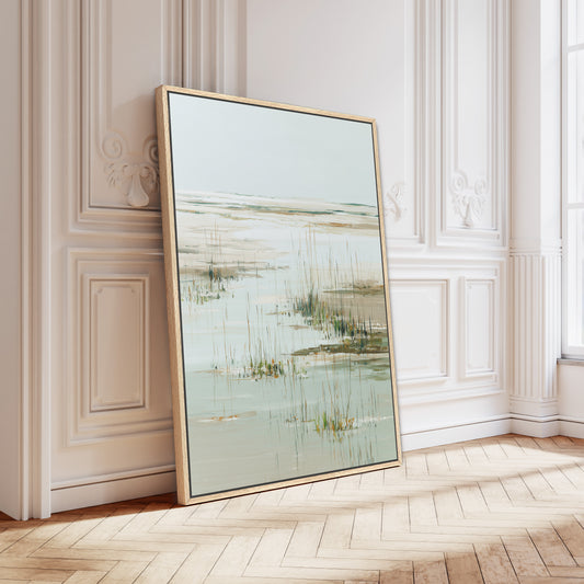 a large framed painting of a serene landscape with a body of water and tall grasses, displayed on a wooden floor against a white wall.