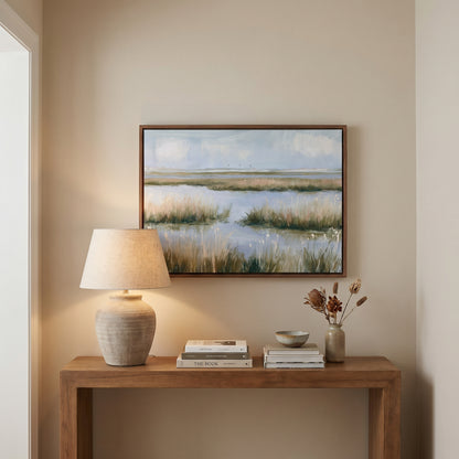 a wooden console table with a lamp, a vase with dried flowers, and a framed landscape painting hanging above it.