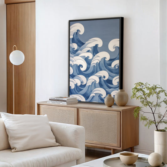 a living room with a large blue and white wave-patterned painting hanging on the wall above a wooden cabinet. The cabinet has two vases on top, and there is a white sofa in the foreground. The room also includes a potted plant and some books, creating a cozy and inviting atmosphere.