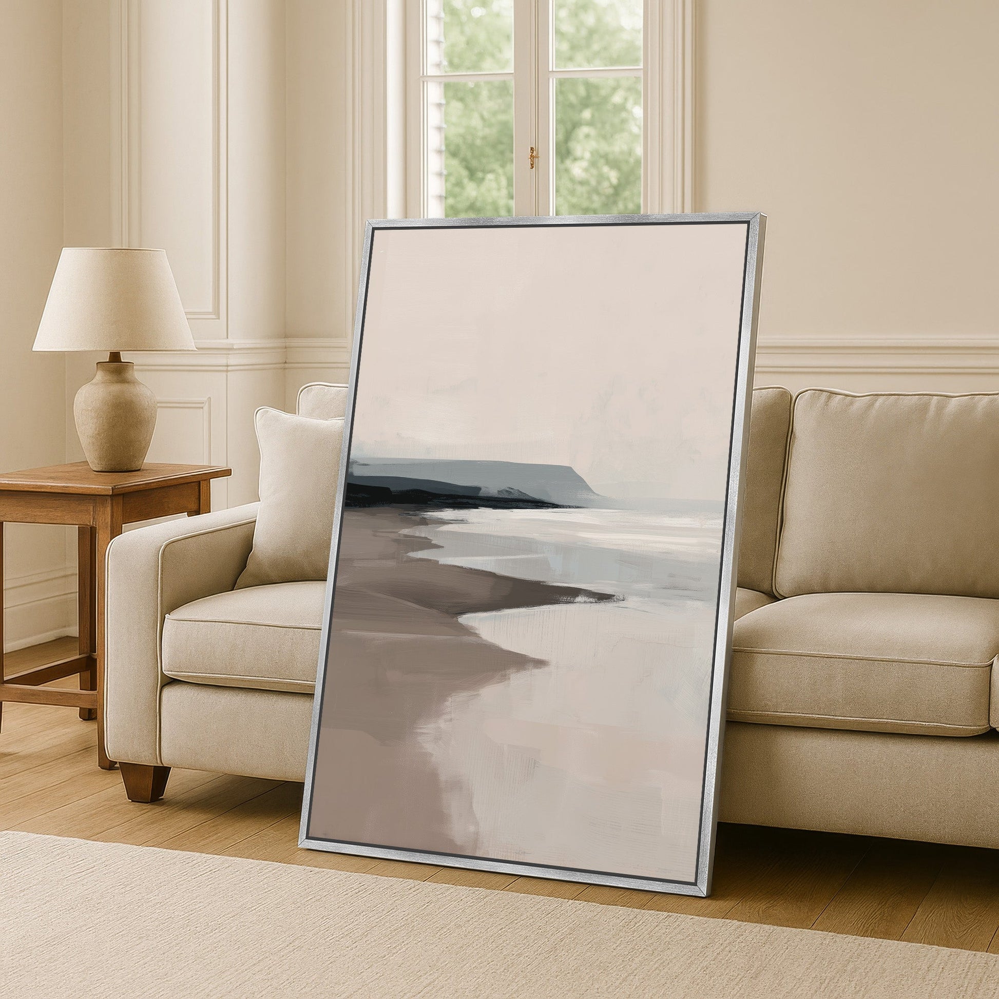 Minimalist coastal seascape in soft beige and gray tones Mel Canvas Print leaned against beige sofa in modern living room