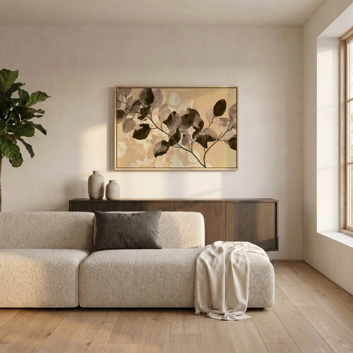 a modern living room with a large, beige sofa and a wooden cabinet. Above the sofa, there is a framed artwork featuring a plant-like design in shades of brown and beige. The room has a clean, minimalist aesthetic with white walls and a wooden floor.