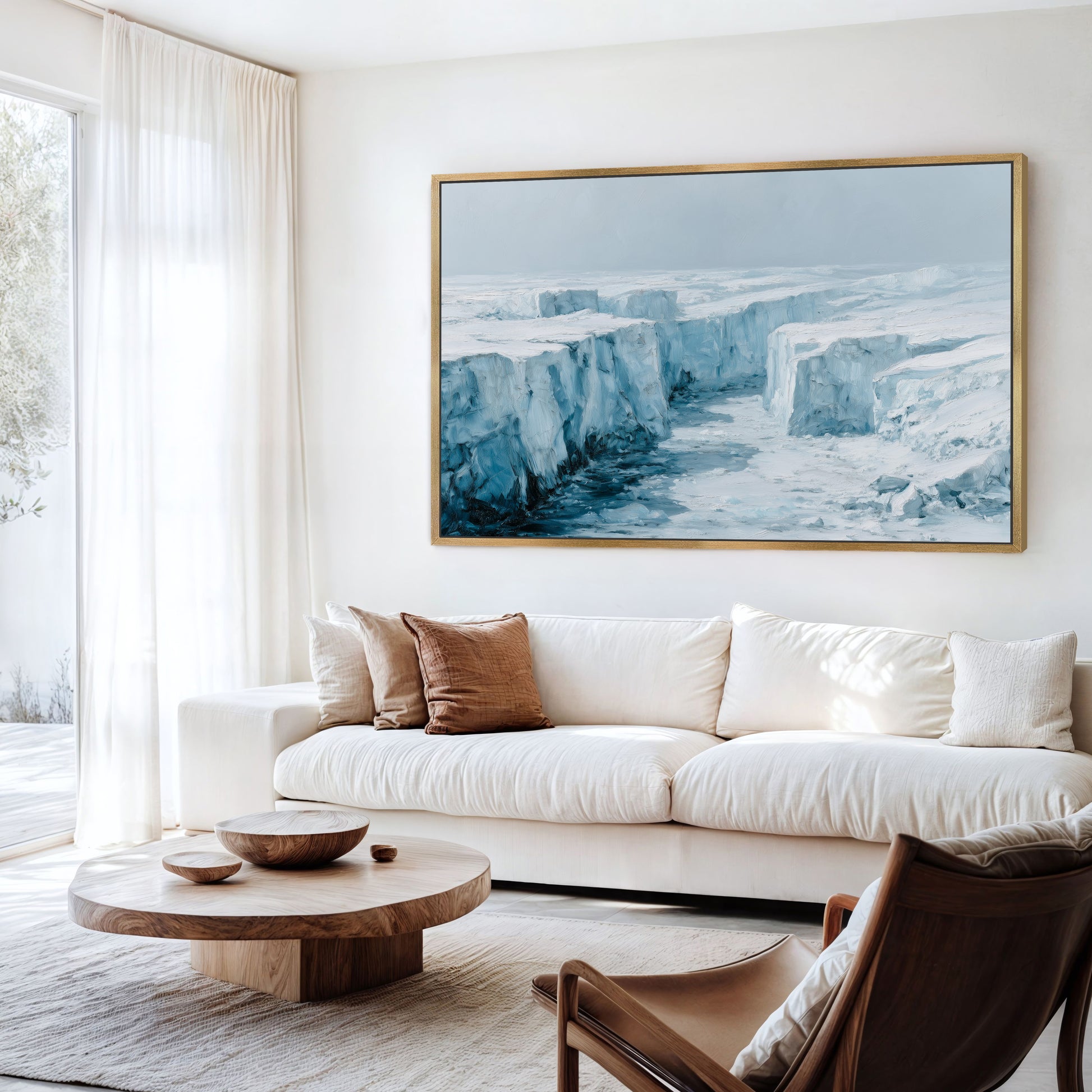 a living room with a large, framed painting of a snowy, icy landscape hanging on the wall above a white sofa. The room has a wooden coffee table in front of the sofa, and a brown leather armchair is situated nearby. The overall decor has a modern and minimalist aesthetic.