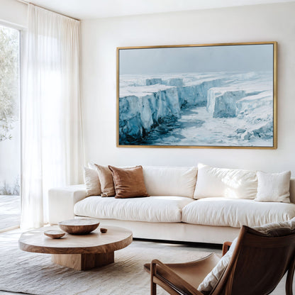 a living room with a large, framed painting of a snowy, icy landscape hanging on the wall above a white sofa. The room has a wooden coffee table in front of the sofa, and a brown leather armchair is situated nearby. The overall decor has a modern and minimalist aesthetic.