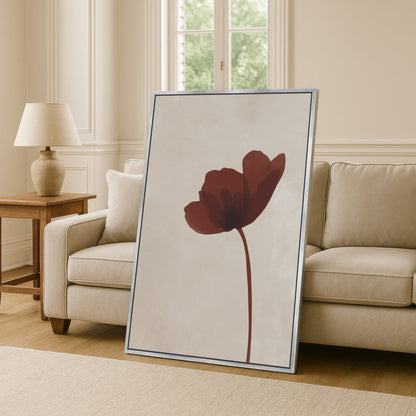 Minimalist Stem Canvas Print featuring a single burgundy flower on a neutral background, framed and leaning against a beige sofa in a modern living room.