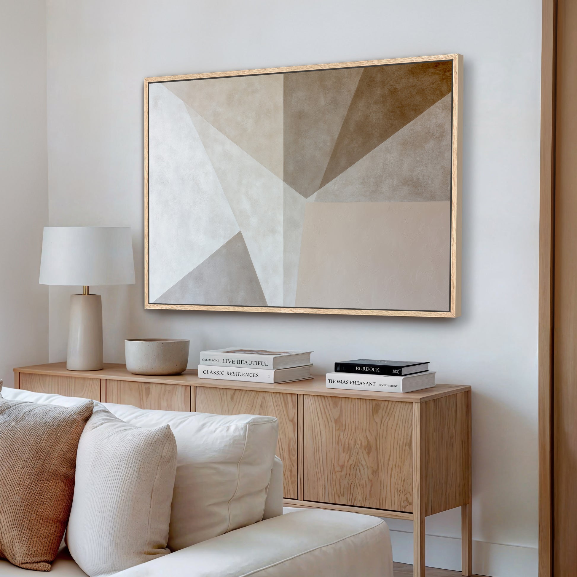 a modern living room with a large abstract painting hanging on the wall above a wooden cabinet. The cabinet has a bowl and a stack of books on top. The room has a white sofa and a wooden coffee table, creating a minimalist and elegant atmosphere.