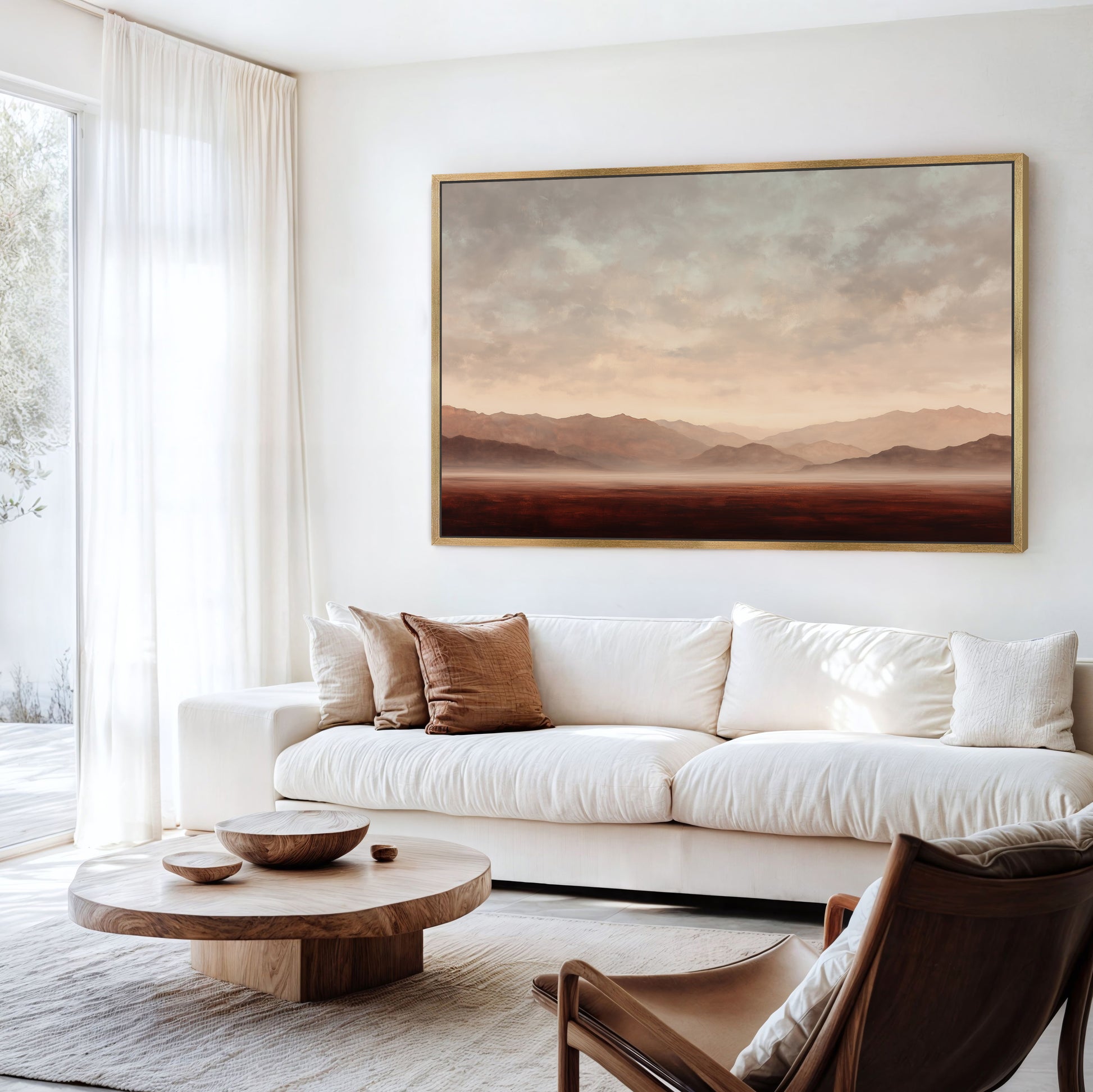 a serene living room with a large landscape painting hanging on the wall above a white sofa. The room is furnished with a wooden coffee table, a brown leather armchair, and a wooden side table. The overall color scheme of the room is neutral, with the brown leather armchair and wooden coffee table adding a touch of warmth to the space.