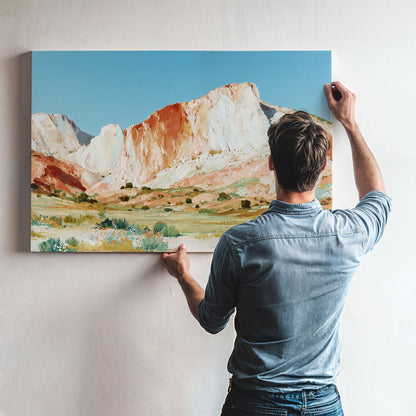 A man is hanging a large landscape painting on a wall, which depicts a mountainous, desert-like scene with a blue sky and colorful vegetation.