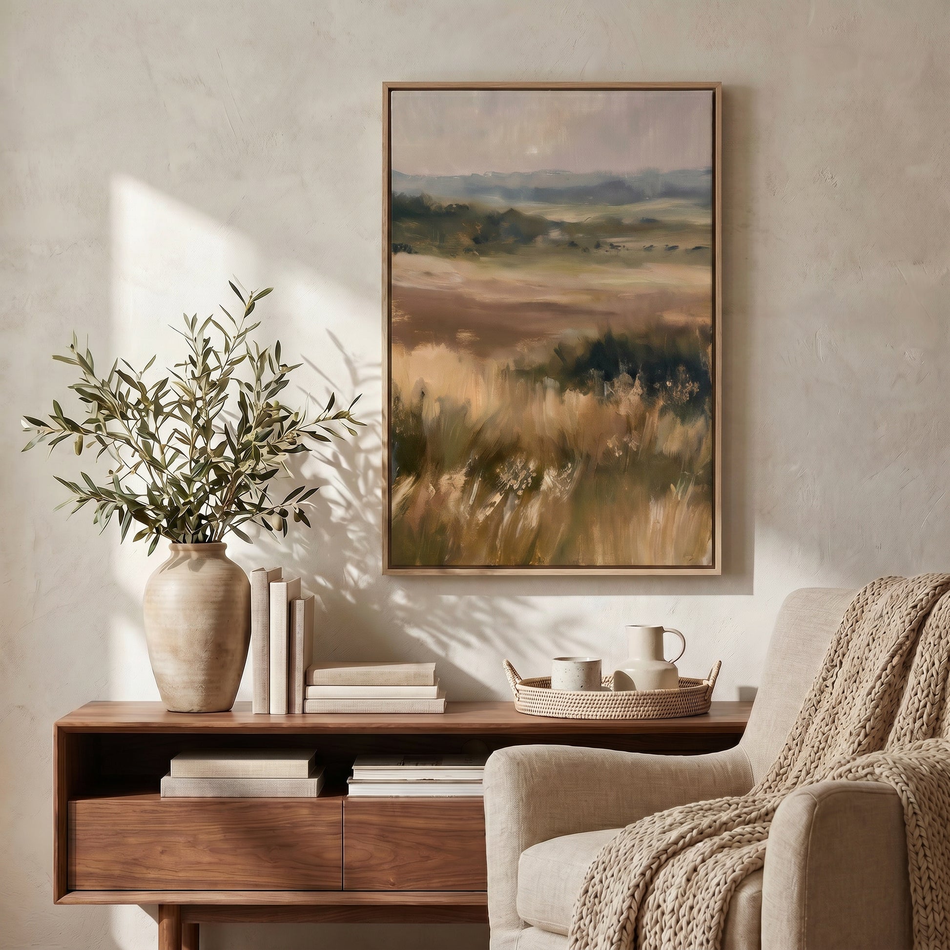 a serene living room with a large landscape painting hanging on the wall, a wooden side table with a vase of greenery and books, and a beige armchair with a cozy blanket draped over it.