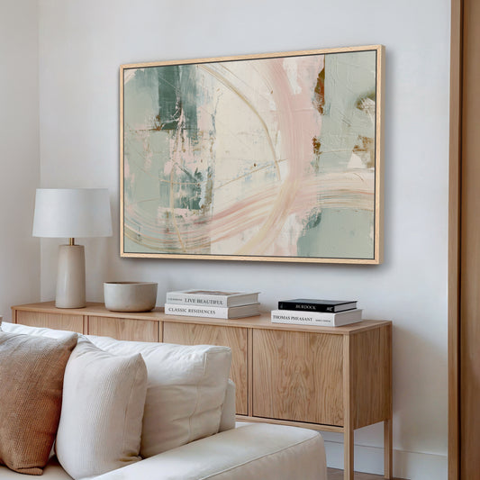 a living room with a large abstract painting hanging on the wall above a wooden cabinet. The cabinet has a bowl and a stack of books on top. The room also includes a white couch and a lamp.
