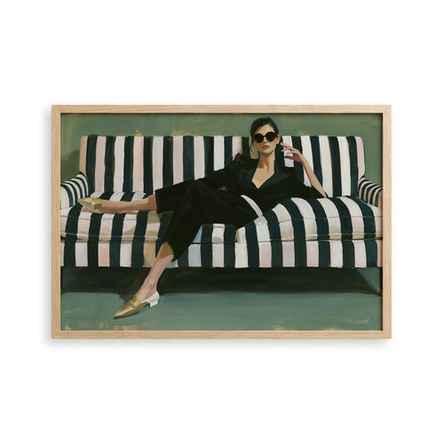 A woman in a black jumpsuit is sitting on a striped couch, wearing gold shoes and sunglasses.
