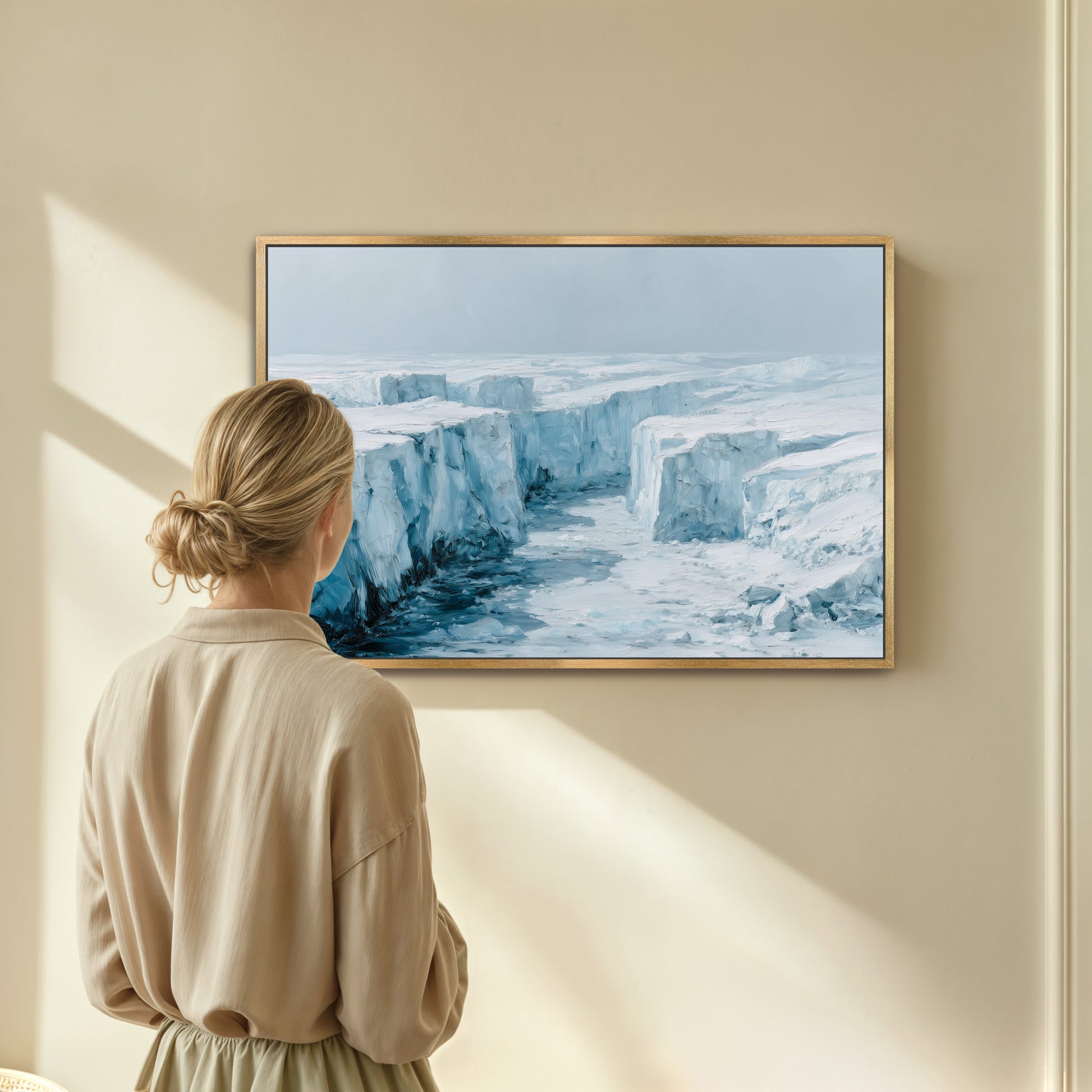 A woman is standing in front of a painting that depicts a snowy, icy landscape with towering cliffs.