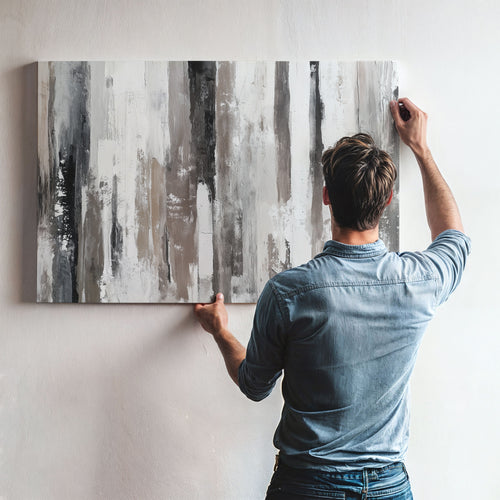 A man is hanging a large abstract painting on a wall.