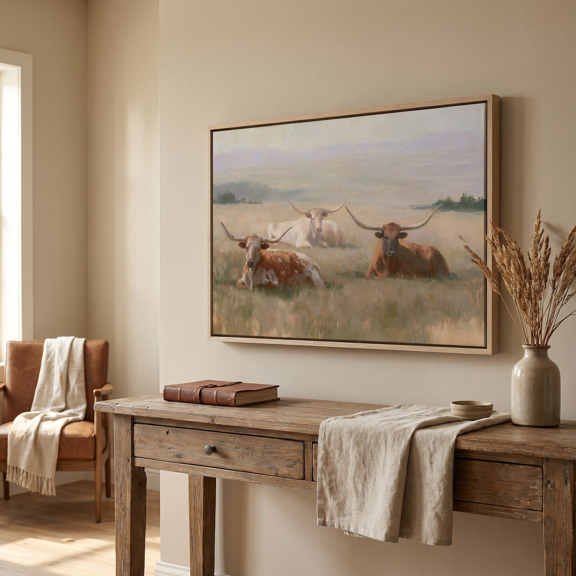 a large painting of longhorns resting in a field, hanging on a wall above a wooden console table.