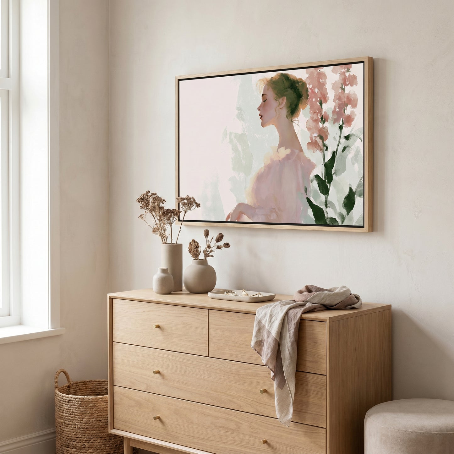 a wooden dresser with a framed painting of a woman's profile hanging above it. The dresser has three drawers and a small table with a vase and dried flowers on it. There is also a woven basket next to the dresser.