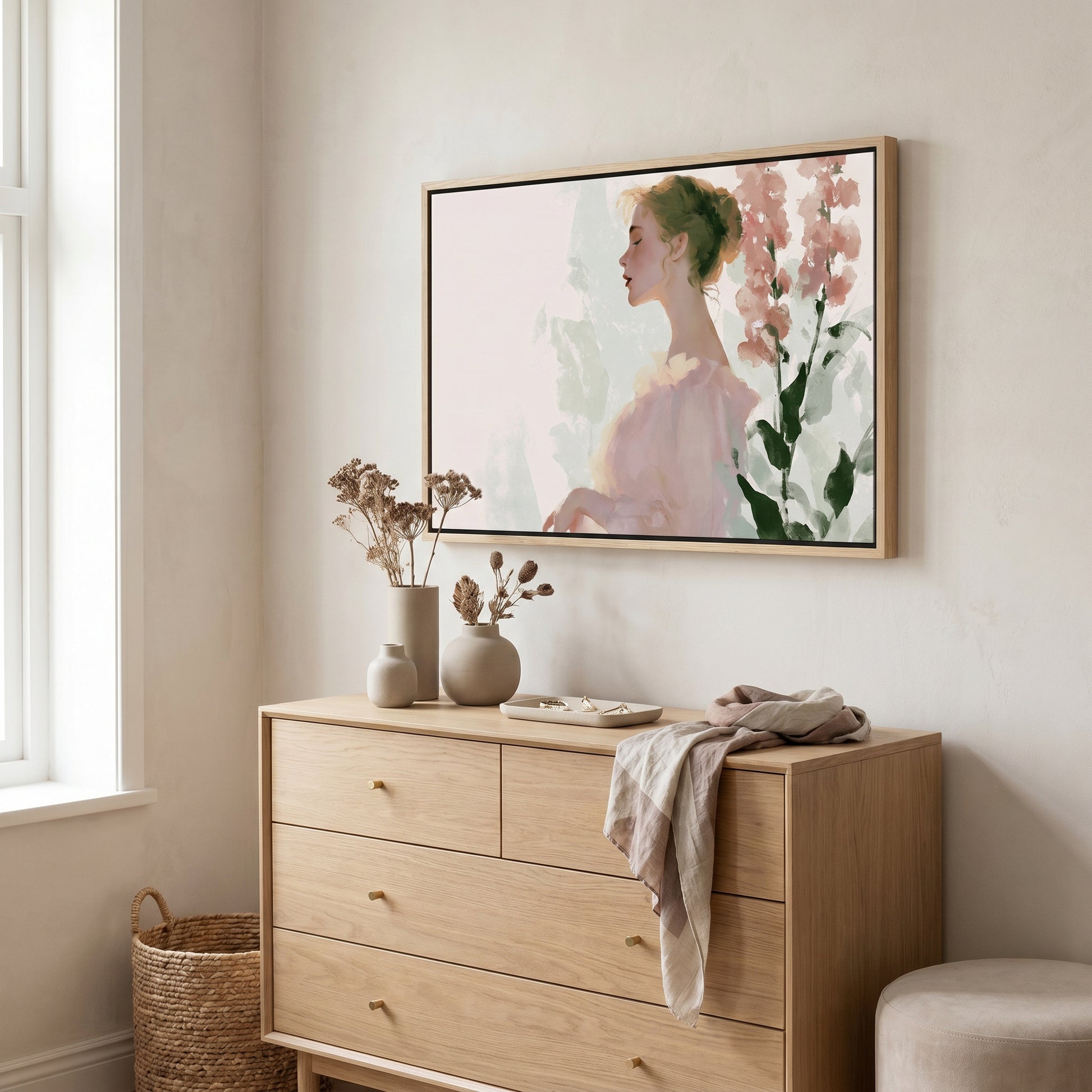 a wooden dresser with a framed painting of a woman's profile hanging above it. The dresser has three drawers and a small table with a vase and dried flowers on it. There is also a woven basket next to the dresser.