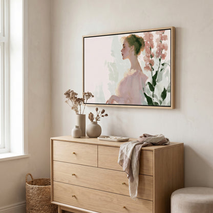 a wooden dresser with a framed painting of a woman's profile hanging above it. The dresser has three drawers and a small table with a vase and dried flowers on it. There is also a woven basket next to the dresser.
