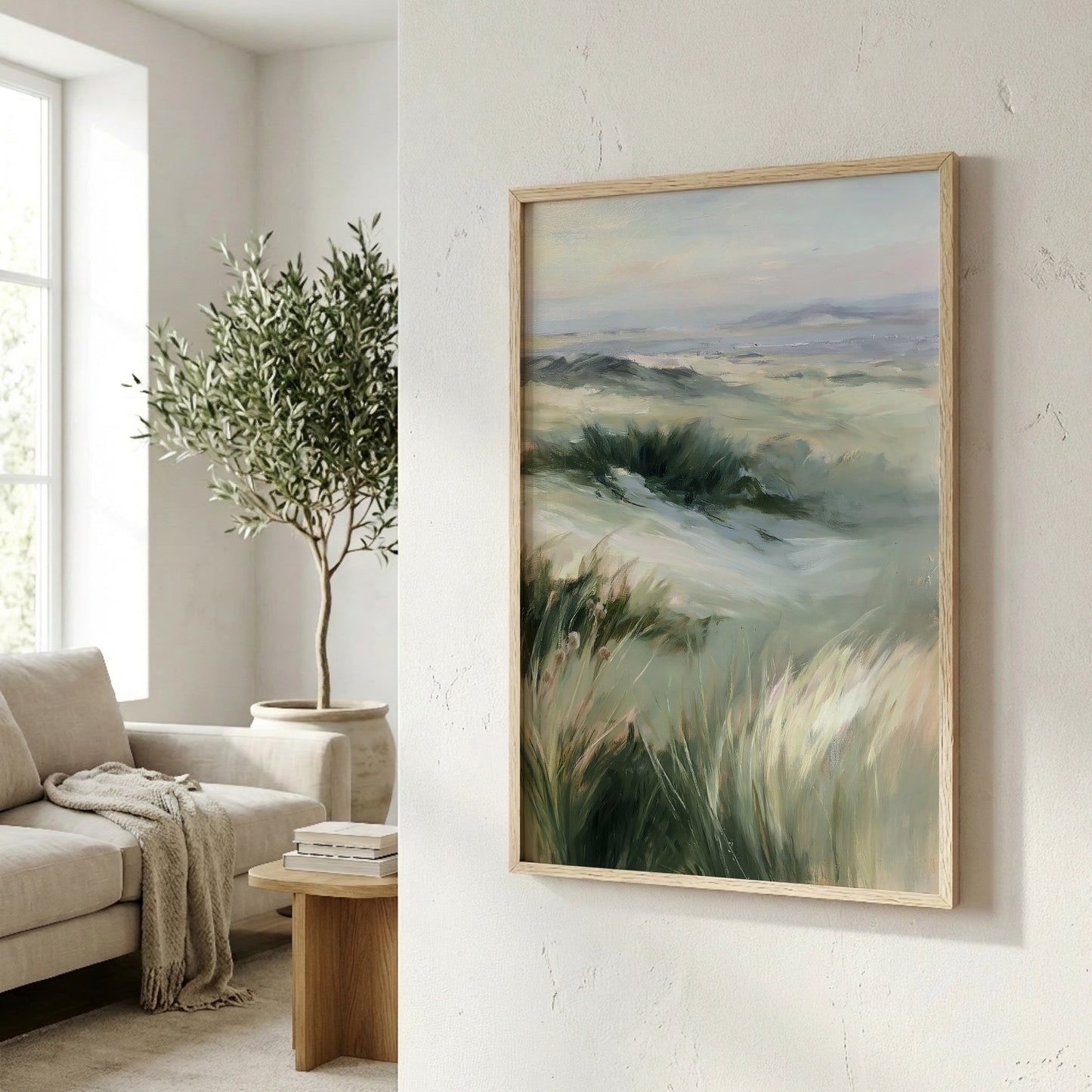 a living room with a large painting of a grassy field hanging on the wall. The painting is framed in a wooden frame and appears to be a landscape artwork. In the background, there is a window that allows natural light to enter the room, and a potted plant is visible on the left side of the image.