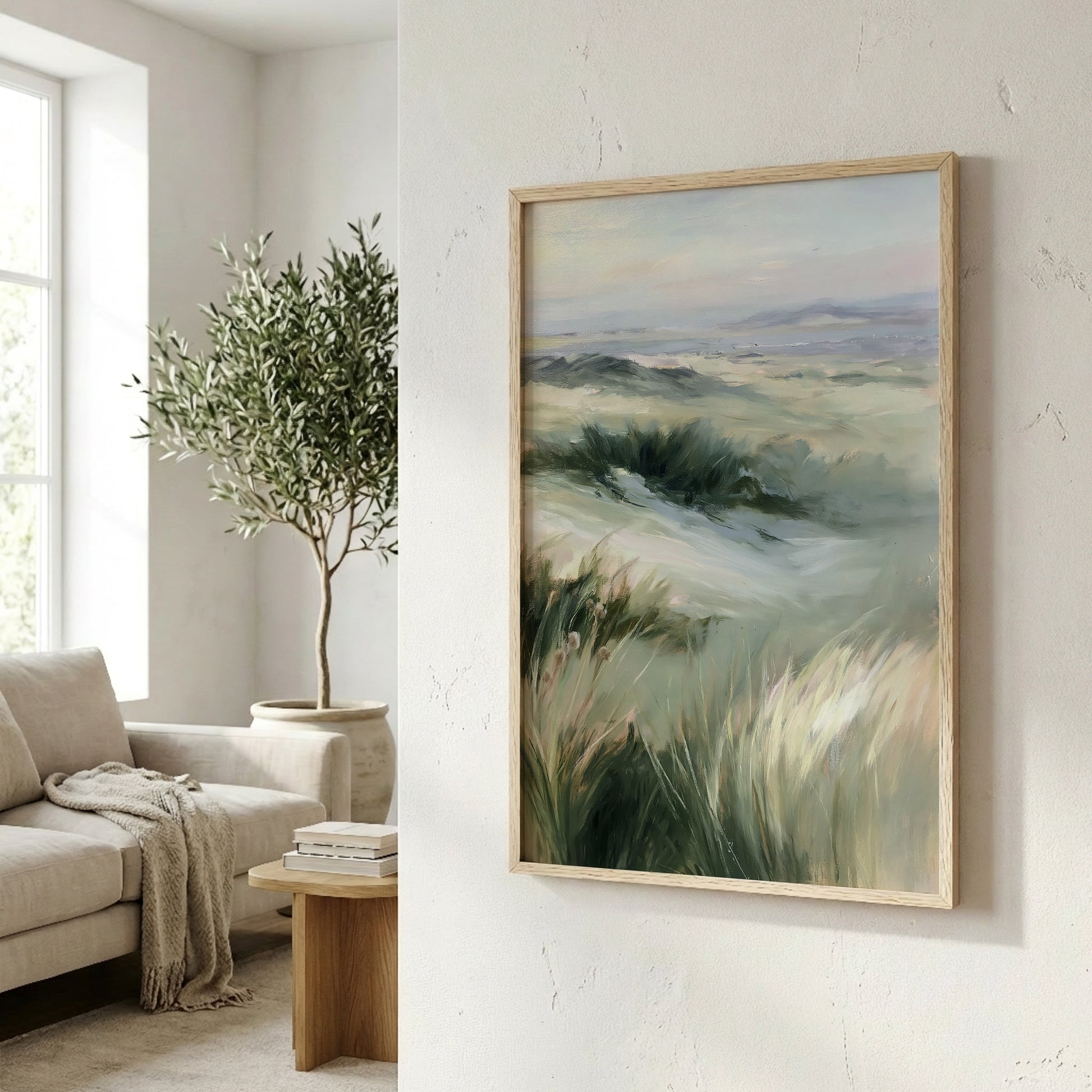 a living room with a large painting of a grassy field hanging on the wall. The painting is framed in a wooden frame and appears to be a landscape artwork. In the background, there is a window that allows natural light to enter the room, and a potted plant is visible on the left side of the image.