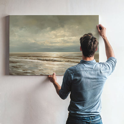 A man hangs a large painting of a serene ocean scene on a wall.