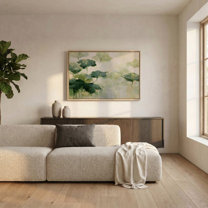 a serene living room with a large, light-colored sofa adorned with a gray throw blanket. Above the sofa, a large painting of green leaves hangs on the wall, adding a touch of nature to the space. The room is well-lit, with natural light streaming in from a window on the right side.