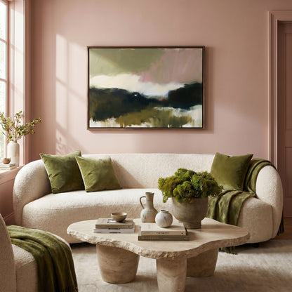 a cozy living room with a large abstract painting on the wall, a white sofa with green throw pillows, a stone coffee table with decorative items, and a window with a plant.