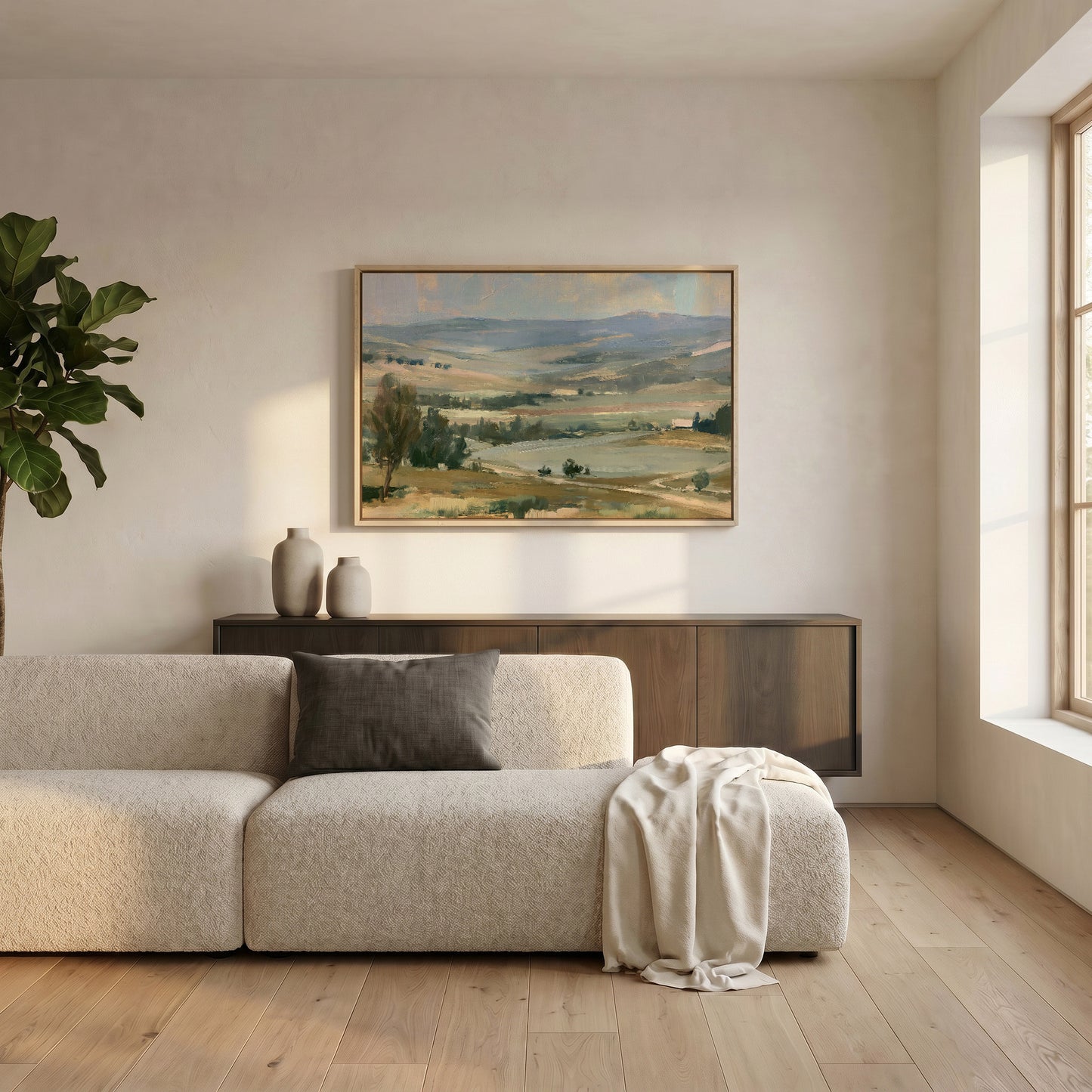 a serene living room with a large landscape painting hanging on the wall above a beige sofa. The sofa is adorned with a gray throw blanket and a white vase, adding a touch of elegance to the space. The room is illuminated by natural light coming through a window, creating a warm and inviting atmosphere.