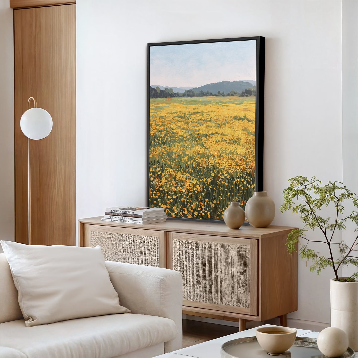 a serene living room with a large framed picture of a field of yellow flowers hanging on the wall, a white sofa, a wooden cabinet, and a potted plant.