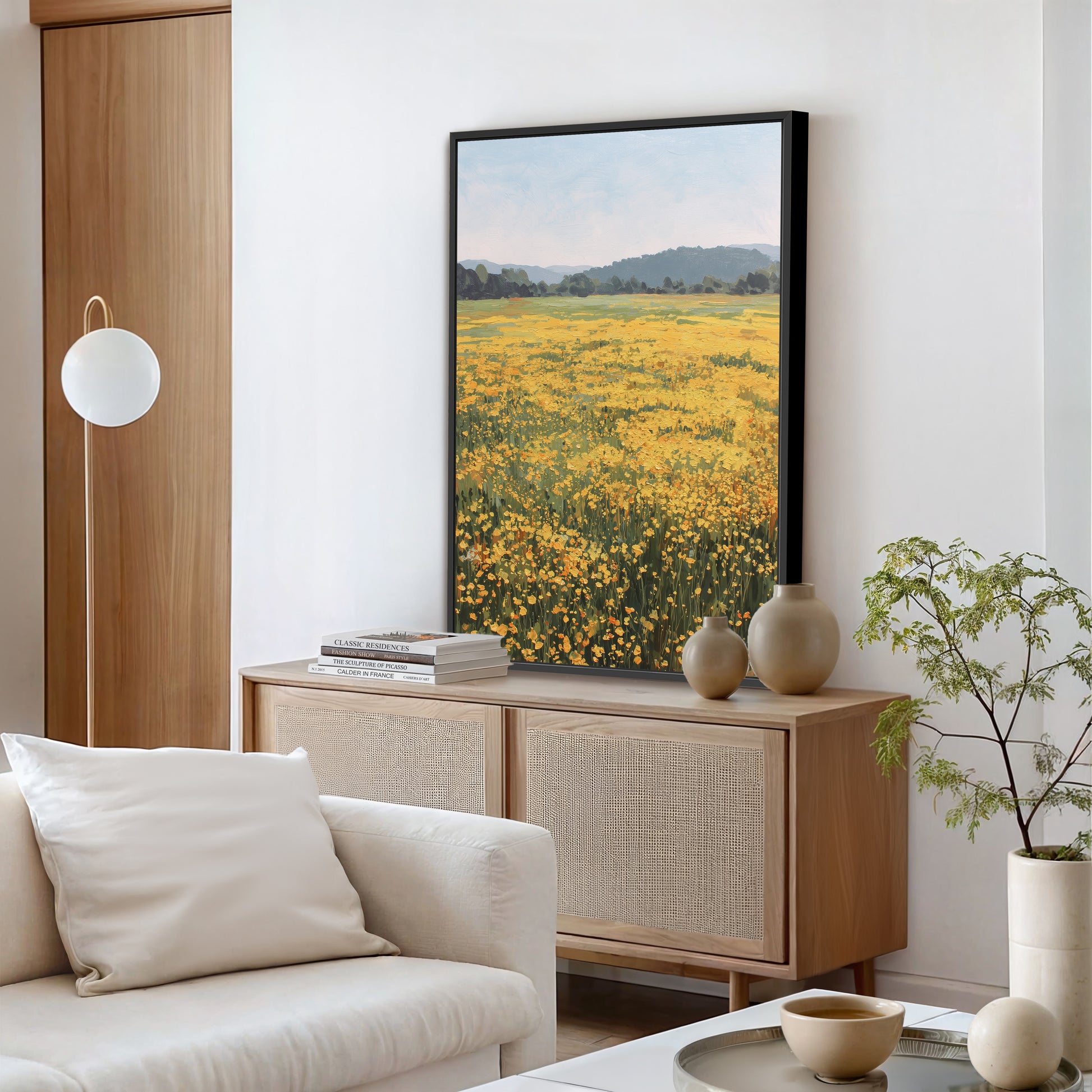 a serene living room with a large framed picture of a field of yellow flowers hanging on the wall, a white sofa, a wooden cabinet, and a potted plant.