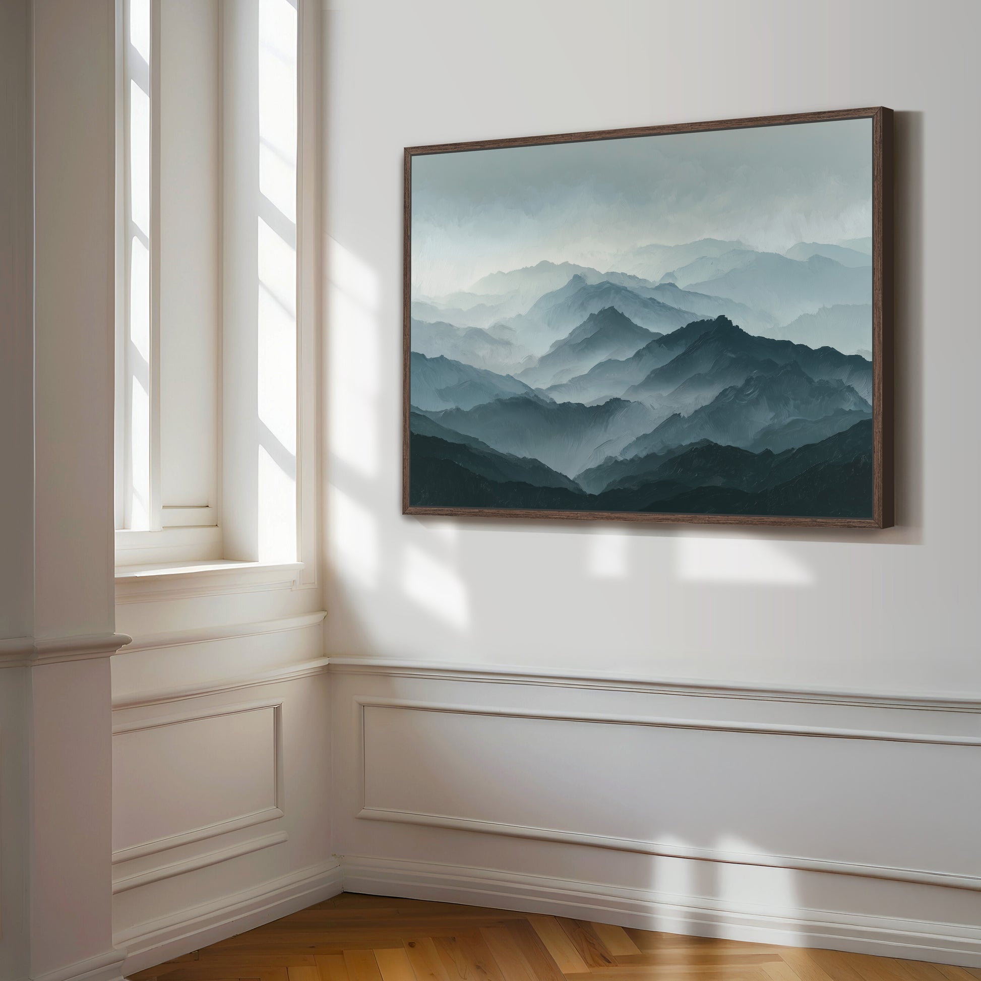 a large framed painting of a mountainous landscape hanging on a white wall in a room with a window.