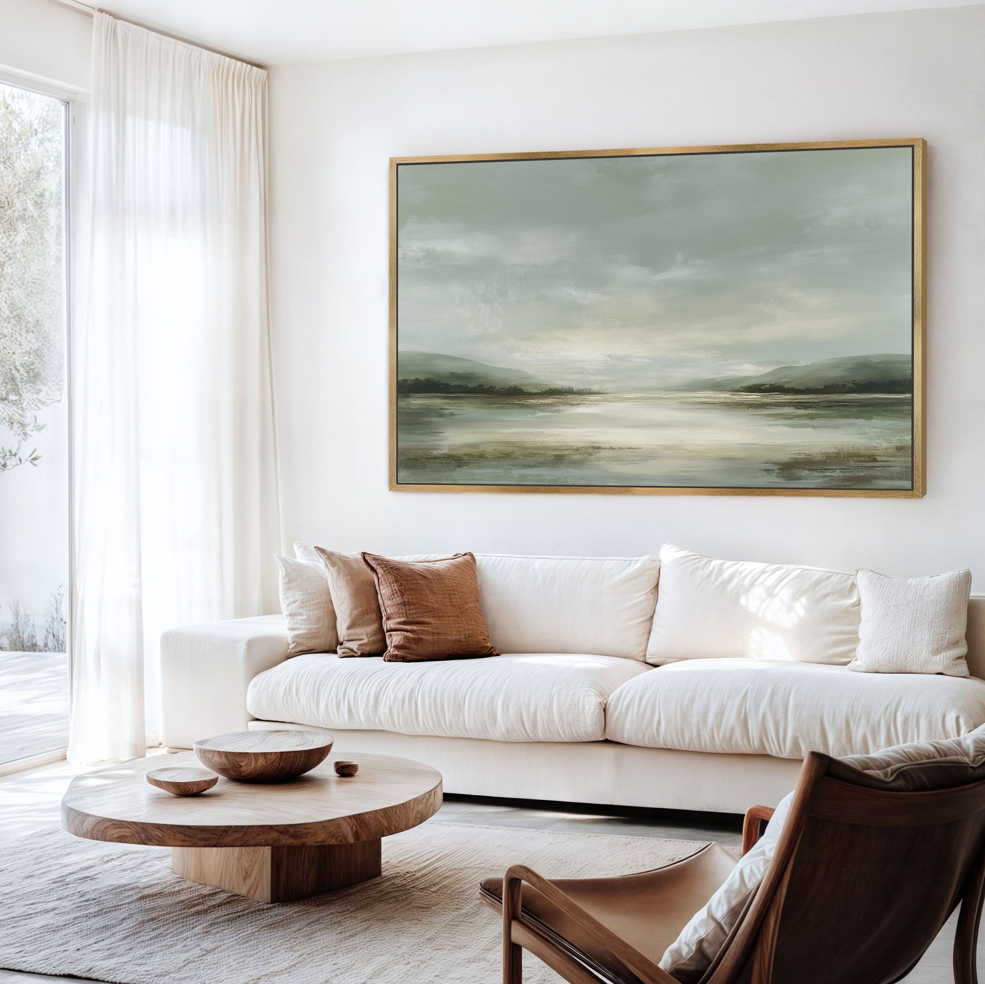 a serene living room with a large landscape painting hanging on the wall above a white sofa. The room is furnished with a wooden coffee table, a brown leather armchair, and a wooden side table. The overall color scheme of the room is predominantly white and brown, creating a warm and inviting atmosphere.