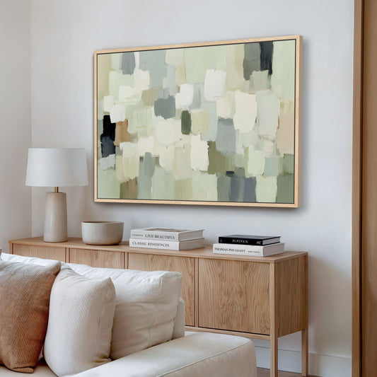 a living room with a large abstract painting hanging on the wall above a wooden console table. The console table has a lamp, a stack of books, and a bowl on it. The room has a white sofa and a wooden floor, creating a cozy and inviting atmosphere.