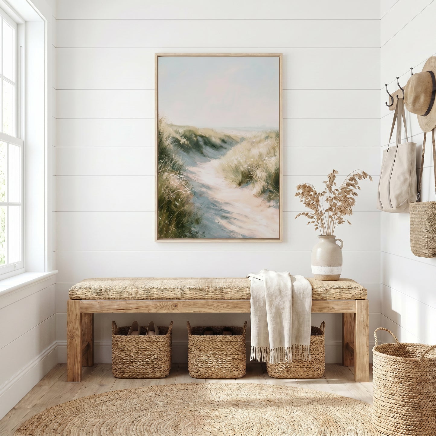 a serene and cozy entryway with a wooden bench, a large framed painting of a beach scene, and a woven basket. The room has white walls and a large window that allows natural light to fill the space.