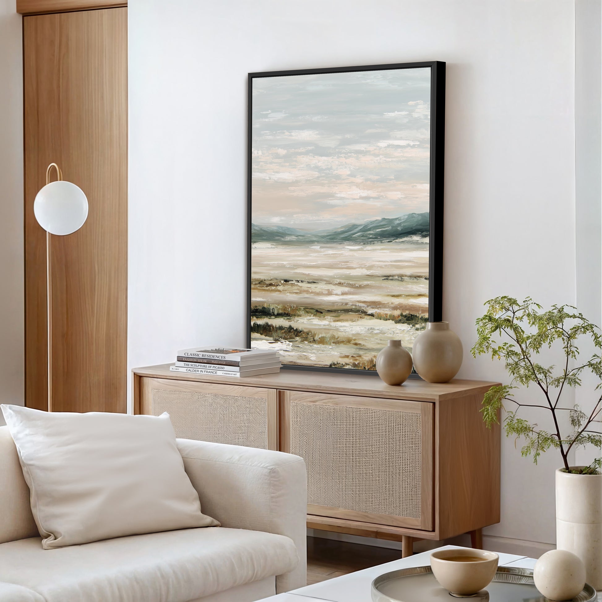 a modern living room with a large landscape painting hanging on the wall, a white sofa, a wooden cabinet, and a potted plant.