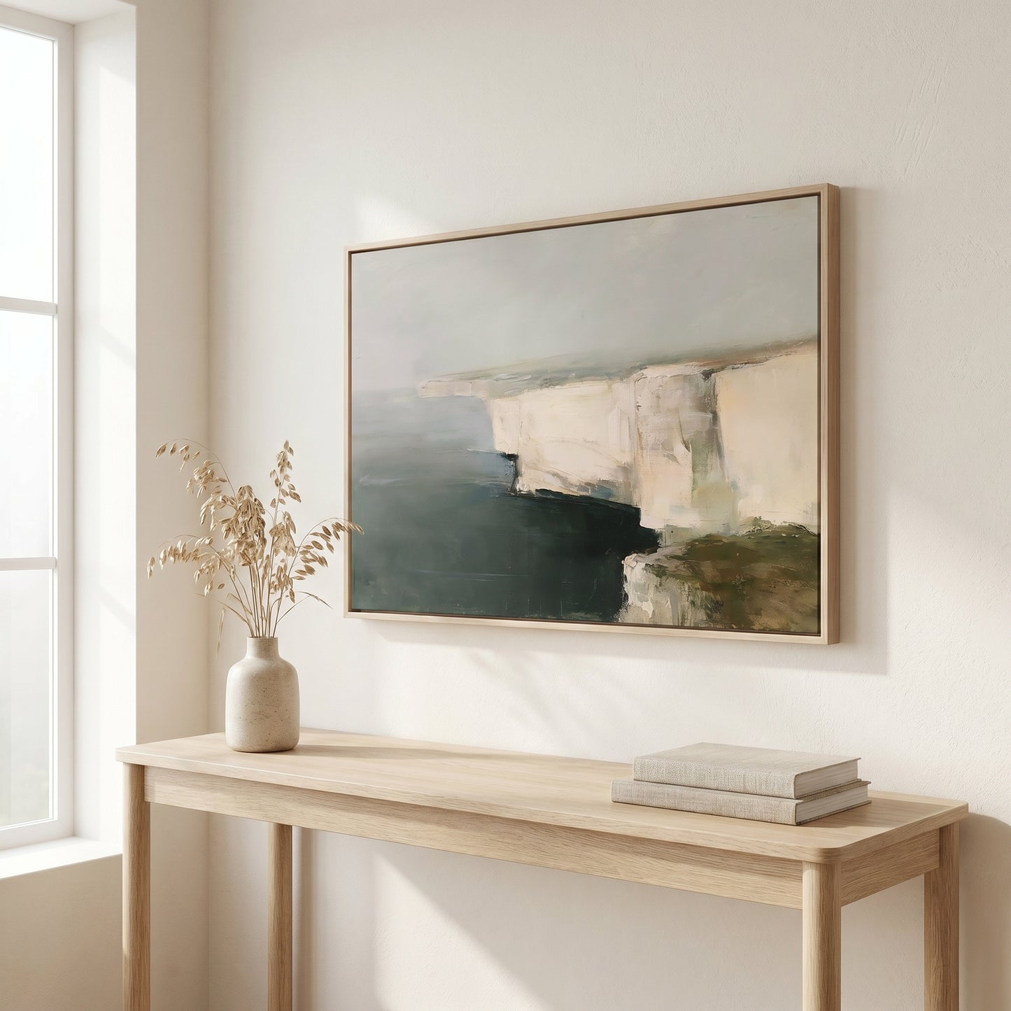 a wooden console table with a vase of dried flowers and a stack of books on it, set against a white wall with a framed landscape painting hanging above it.