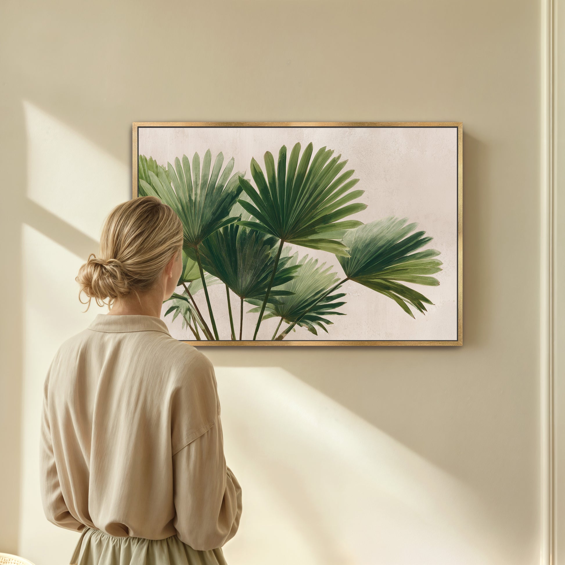 A woman is standing in front of a framed painting of green palm leaves, looking at it with interest.