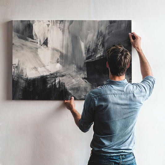 A man is hanging a large abstract painting on a wall.