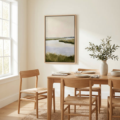 a serene dining room with a wooden table and chairs, a framed landscape painting on the wall, and a vase of greenery on the table.