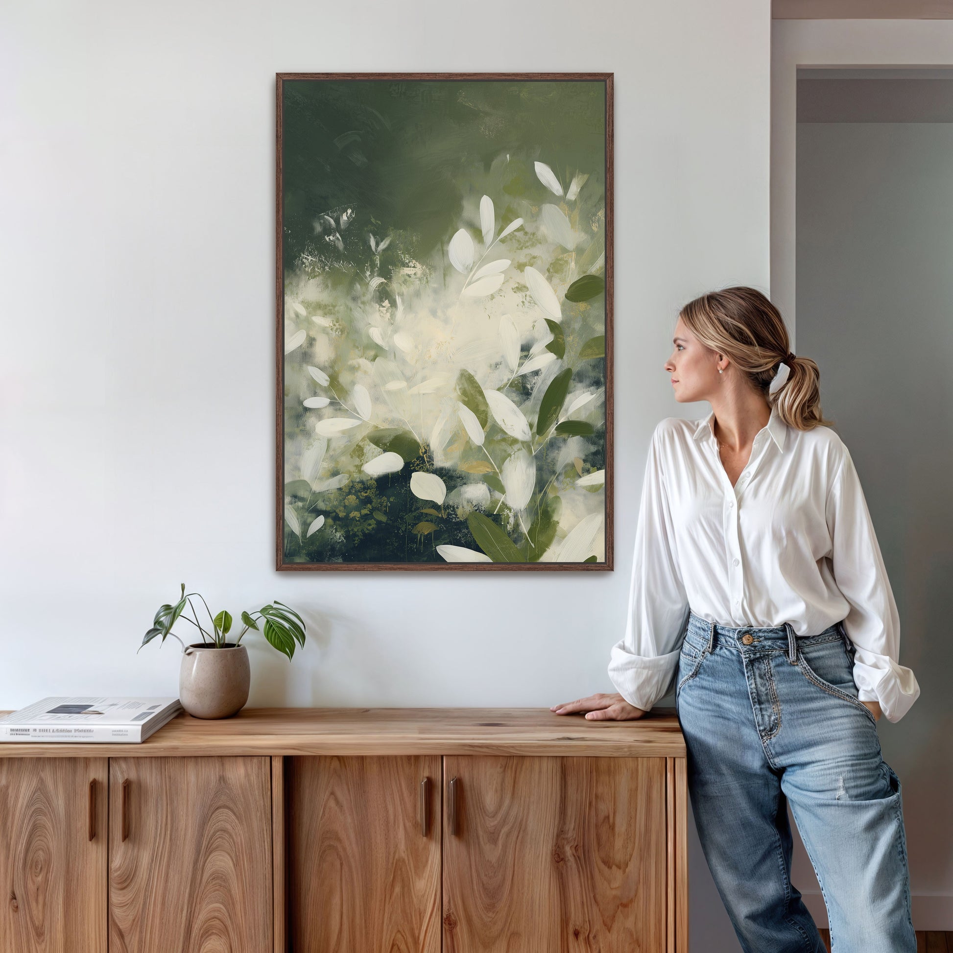 Verdure canvas wall art featuring soft ivory leaves and deep green tones in a modern botanical style hanging above a wooden sideboard in a minimalist interior.