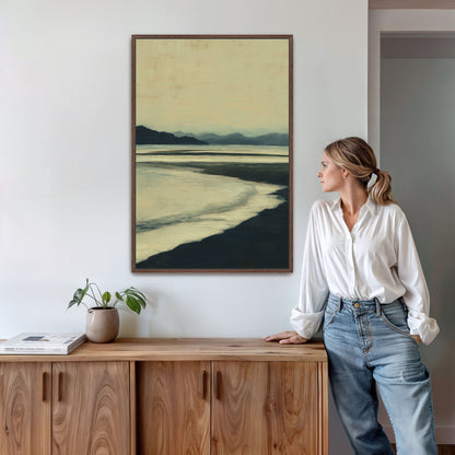 Echoes canvas print of hazy blue and soft ochre shoreline at dusk in a wooden frame on a white wall above wooden cabinet with plant and woman standing nearby