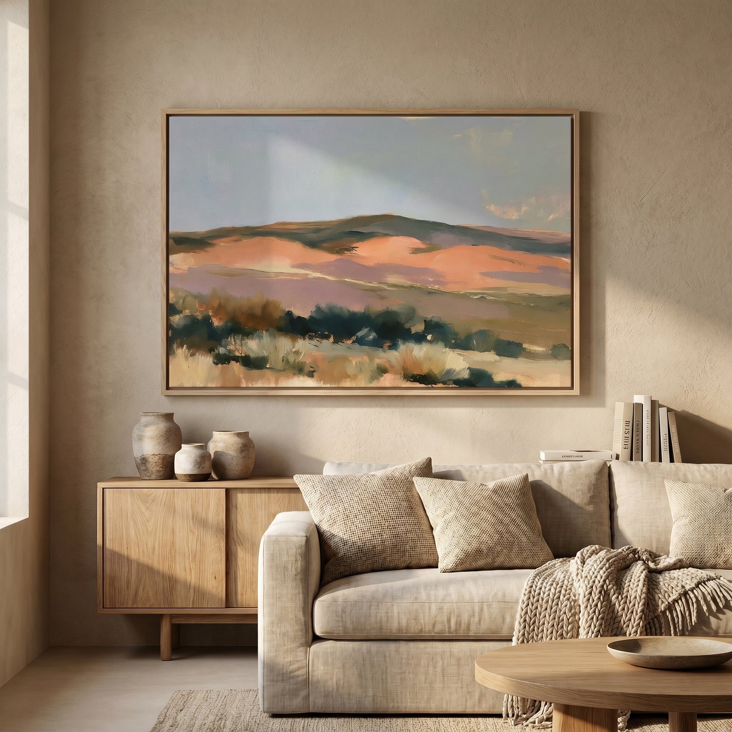 a large, framed painting of a landscape hanging on a wall in a living room. The painting depicts a serene, mountainous scene with a mix of green, orange, and brown colors. The living room has a beige sofa, a wooden coffee table, and a bookshelf filled with books.