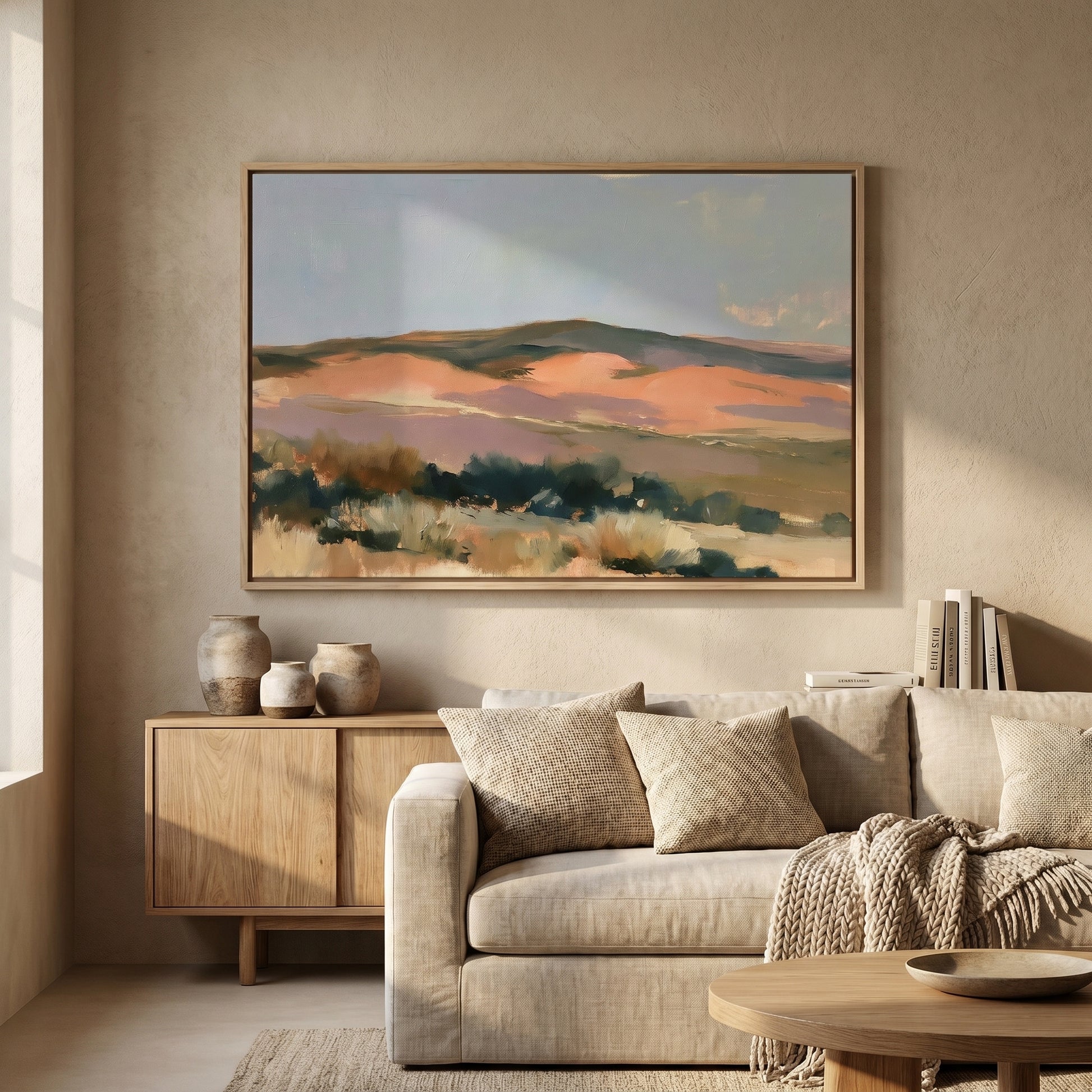 a large, framed painting of a landscape hanging on a wall in a living room. The painting depicts a serene, mountainous scene with a mix of green, orange, and brown colors. The living room has a beige sofa, a wooden coffee table, and a bookshelf filled with books.