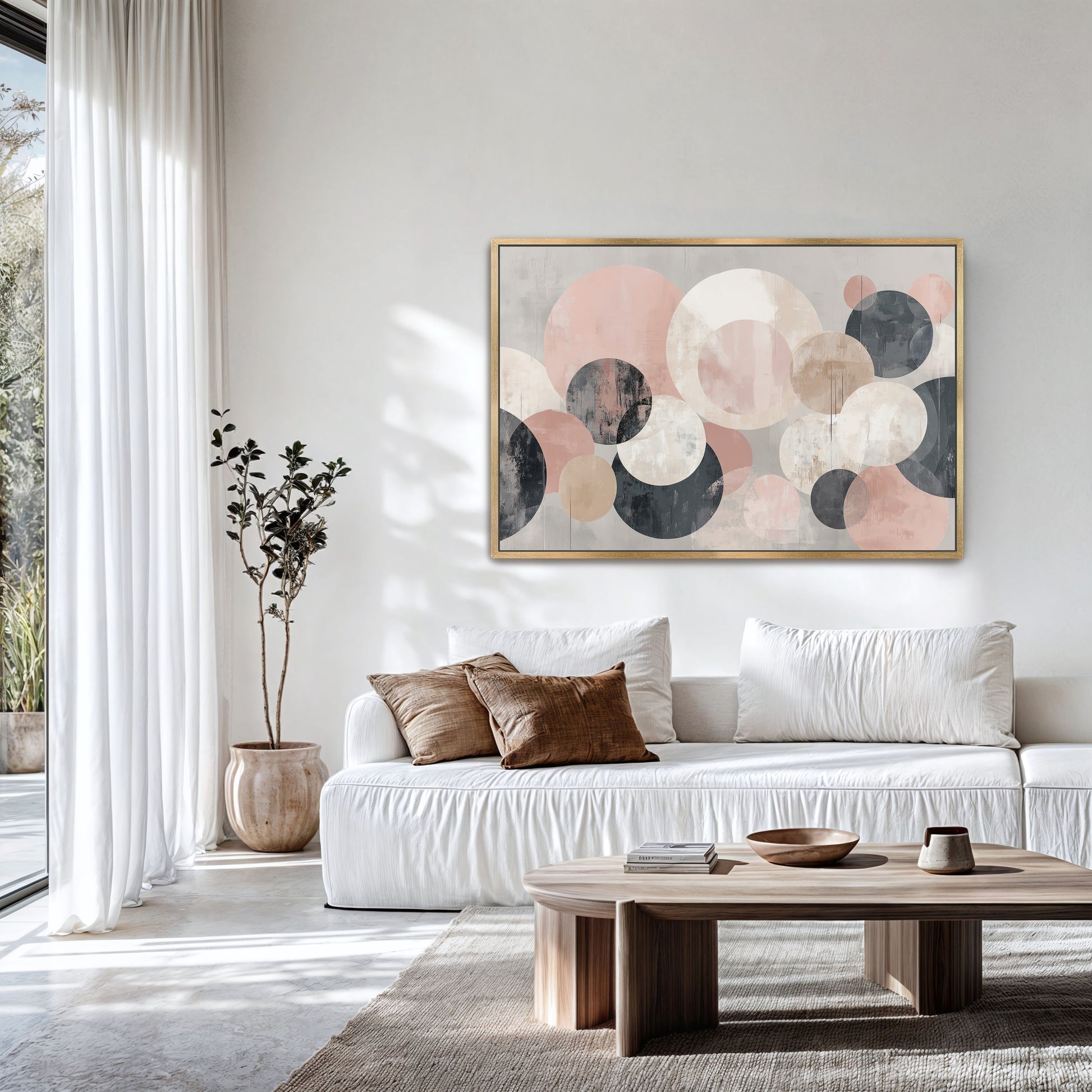 a modern living room with a large abstract painting featuring circles in various shades of pink and gray hanging on the wall above a white sofa. The room has a large window, a wooden coffee table, and a potted plant, creating a cozy and inviting atmosphere.