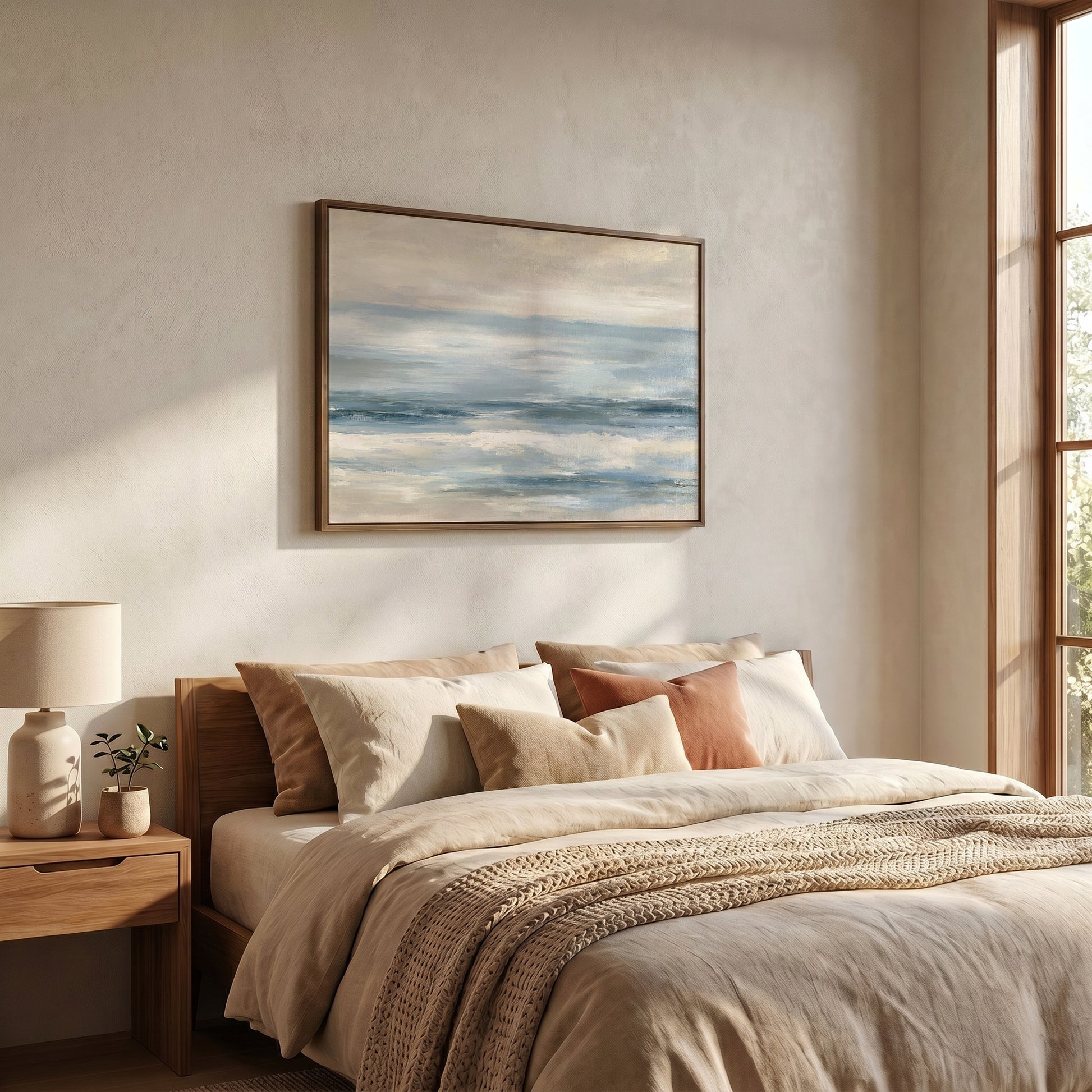 a serene bedroom scene with a large bed adorned with beige bedding and a wooden headboard. Above the bed, a framed painting of a tranquil ocean landscape is displayed on the wall. The room is illuminated by natural light streaming in from a window, creating a warm and inviting atmosphere.