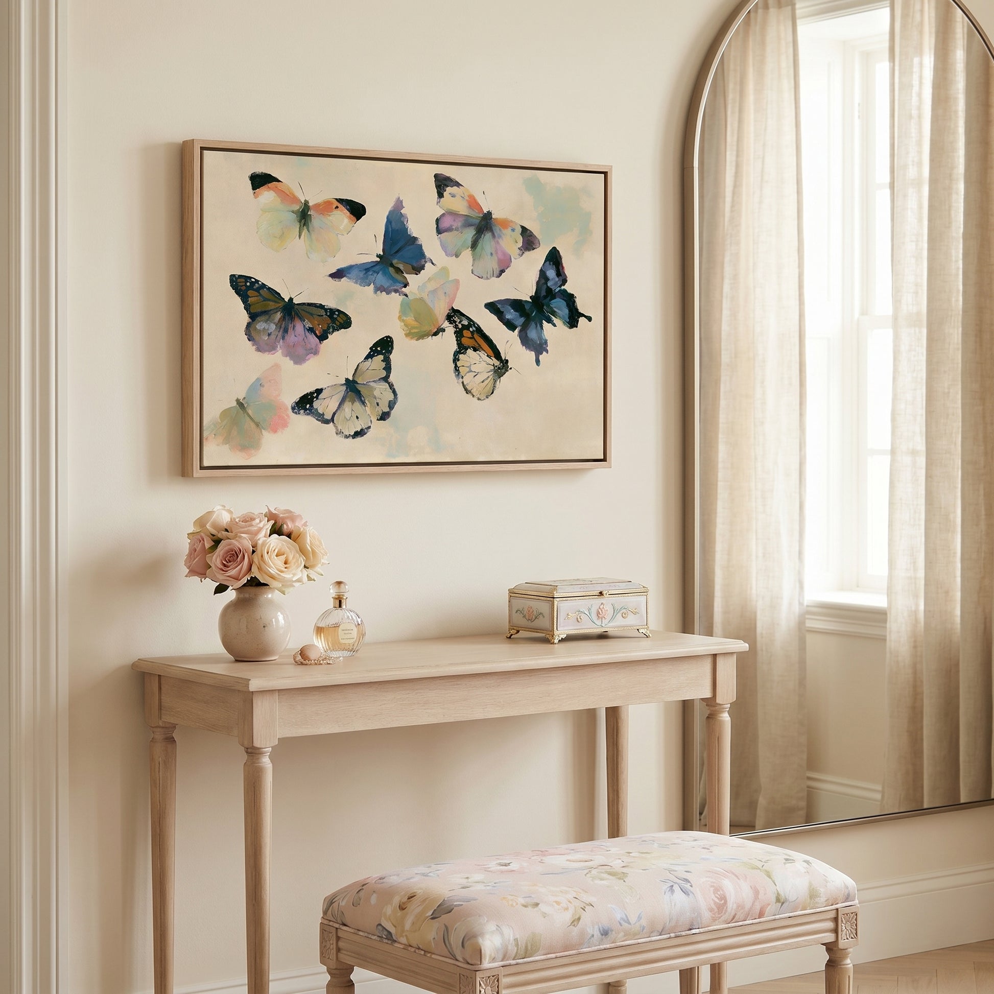 a light-colored wooden table with a vase of flowers, a small box, and a mirror above it. The table is situated in a room with a window and a painting of colorful butterflies hanging on the wall.